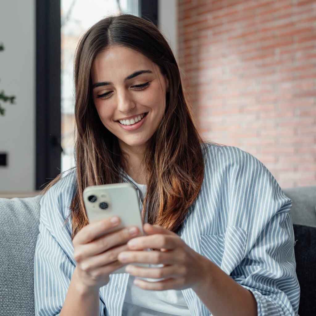 Woman smiles happily at phone as if pleased with customer complaint resolution outcome.