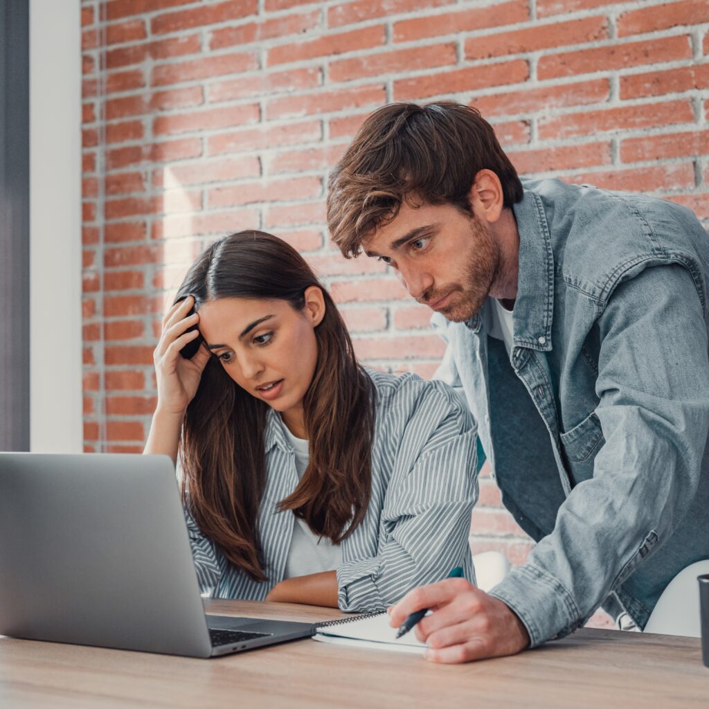 Man and woman look frustratedly at laptop, as if dealing with customer complaints management.